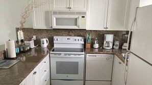 A kitchen with white cabinets, a microwave, a stove, a dishwasher, and a refrigerator. There are decorative shells and a small sailboat on the wall. - Bimini Home at the Beach (Bimini)