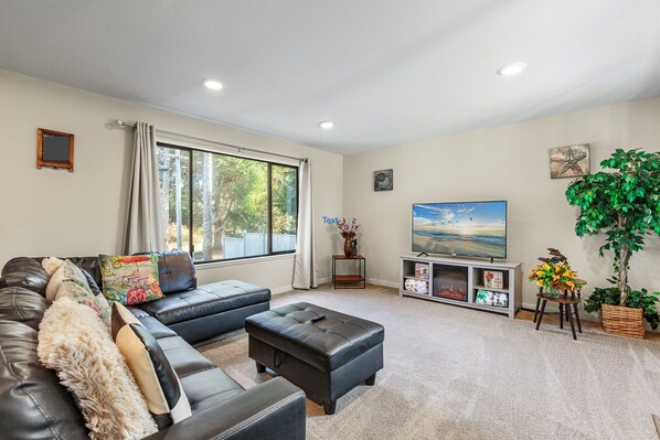 A living room with a sofa, ottoman, TV, and a large window.