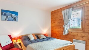 Ein gemütliches Schlafzimmer mit einem hölzernen Bett, einem roten Sessel, einem Fenster mit Vorhängen und einem Bild an der Wand.