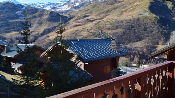 Eine Bergbude mit einer Holzdiele und Blick auf schneebedeckte Berge.