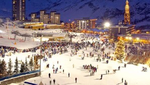 Ein mit Schnee bedeckter Skihang mit einer Menschenmenge, Gebäuden und einem markanten Turm im Hintergrund.