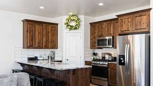 A modern kitchen with wooden cabinets, a stainless steel refrigerator, a microwave, and an island with bar stools. - Libelle Landing by RedAwning (Washington)