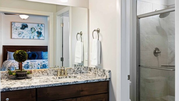 A bathroom with a marble countertop, dark wooden cabinets, a glass shower enclosure, and a large mirror.