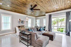 A spacious living room with a high ceiling, a ceiling fan, and large windows.