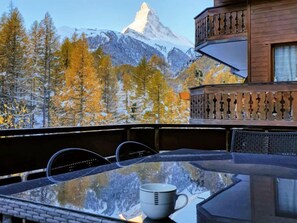 A glass table with a cup, overlooking a mountainous landscape with autumn trees and a snow-capped peak. - Nirwana by Interhome (Zermatt)