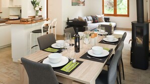 Ett matområde med ett långt bord som är dukat för sex personer, omgivet av stolar. Ett köksområde med vita skåp och en bänkskiva syns till vänster.