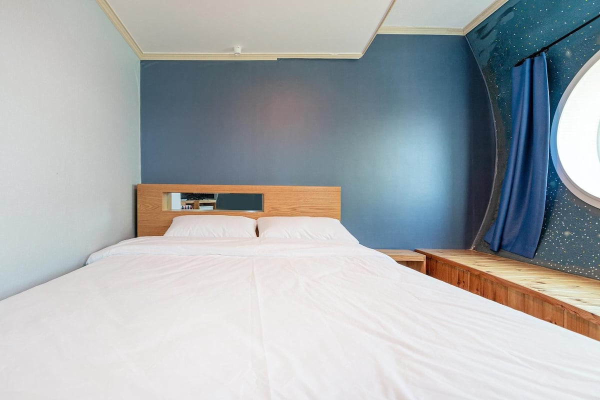 Une chambre à coucher avec un lit, une table de chevet, un miroir et une fenêtre avec des rideaux.