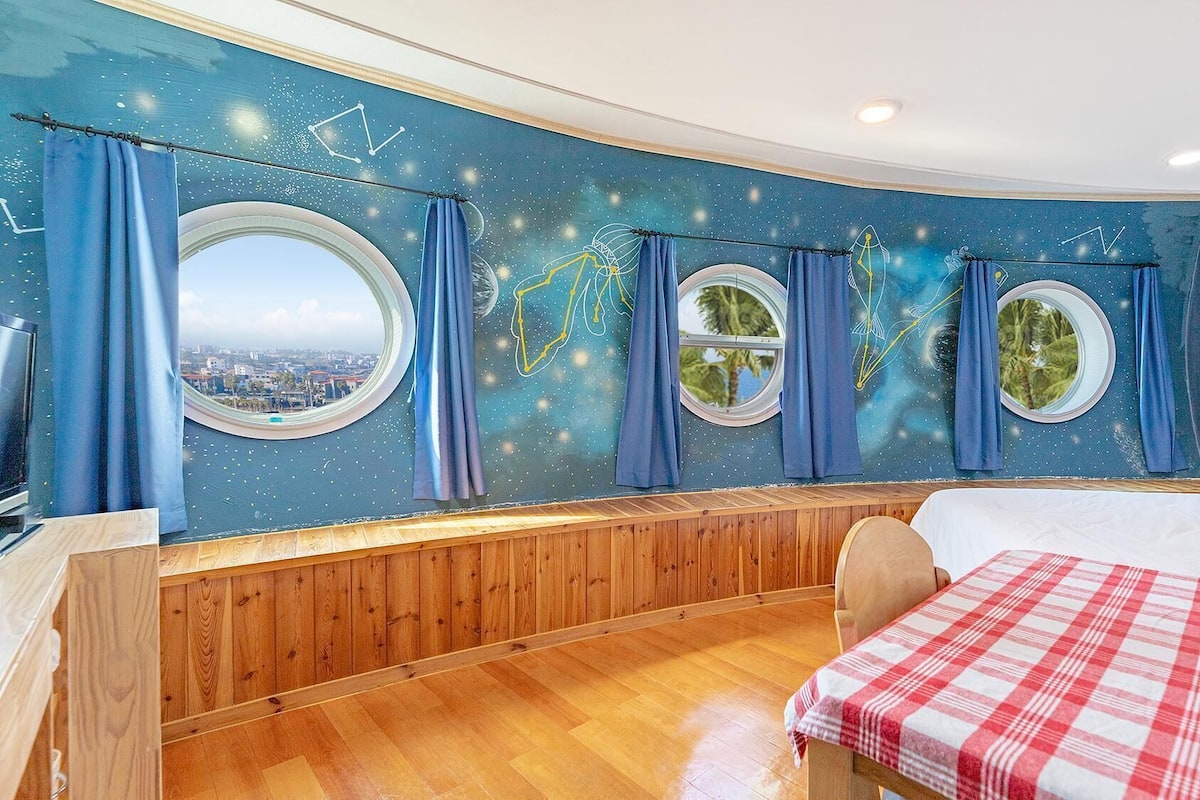 Une chambre avec vue sur la ville, des lambris en bois et une couvre-lit à carreaux.