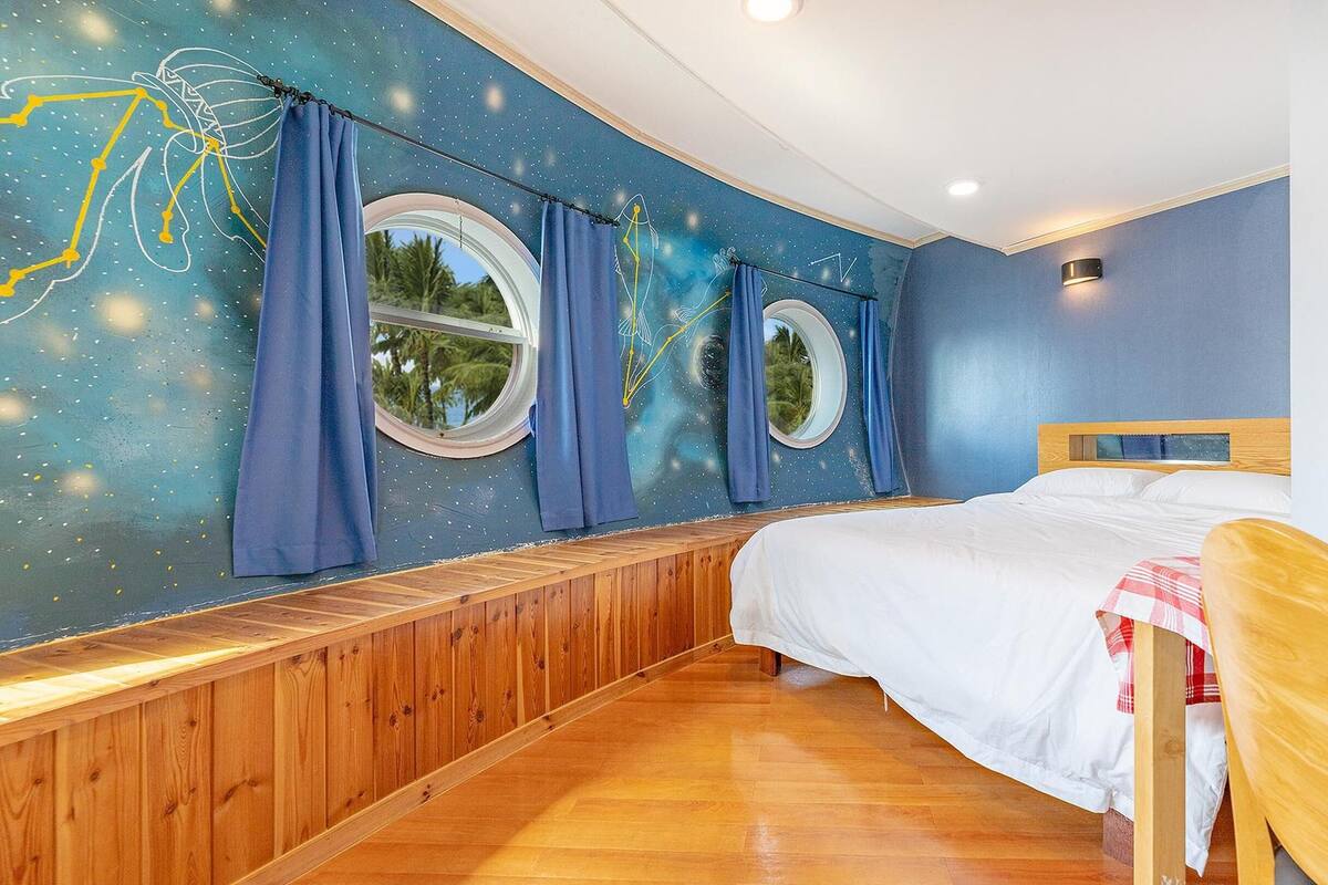 Une chambre avec un plancher en bois, un lit avec une literie blanche et une fenêtre avec des rideaux bleus.