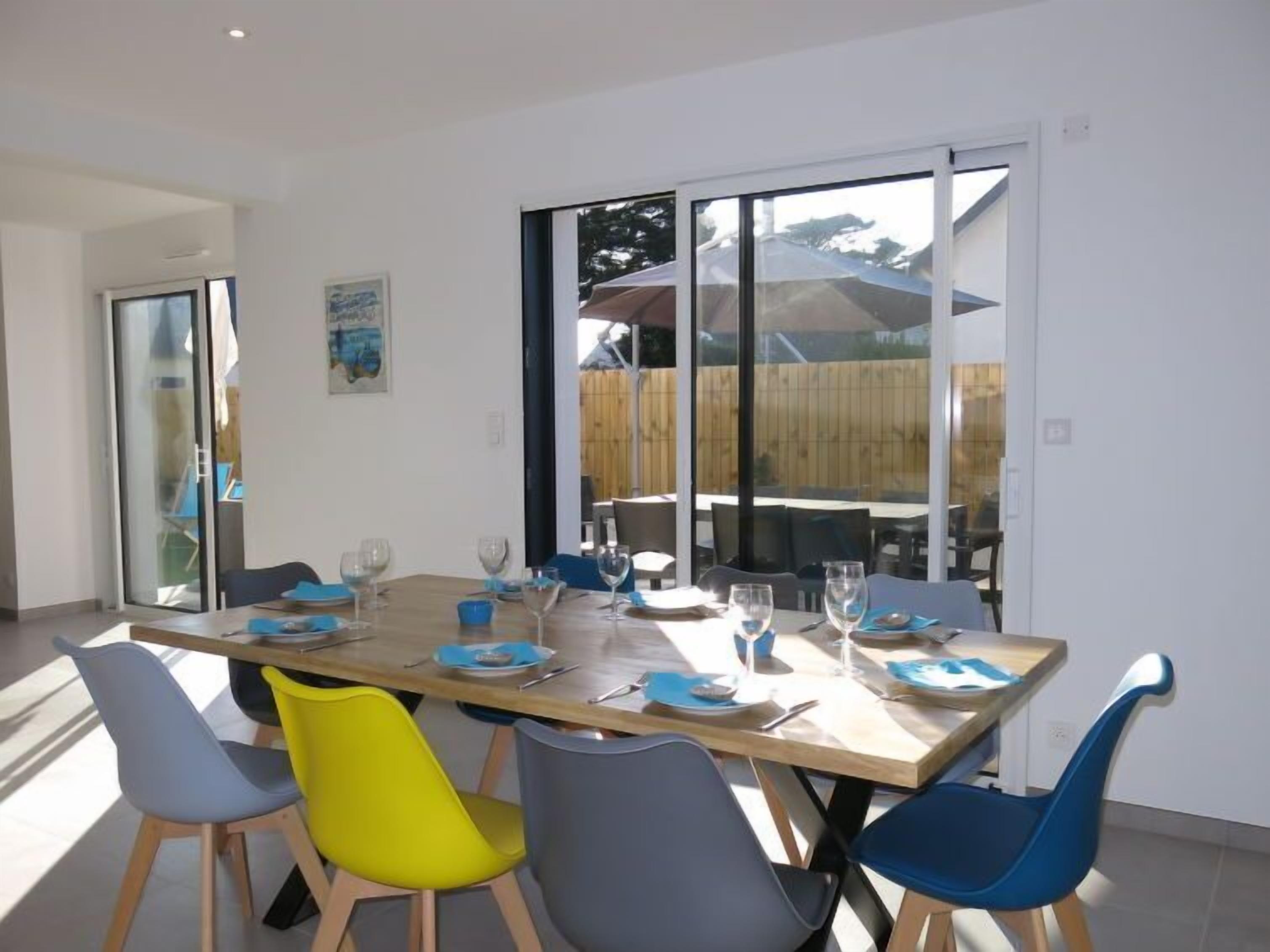 A dining area with a wooden table set for six, surrounded by six chairs in various colors.