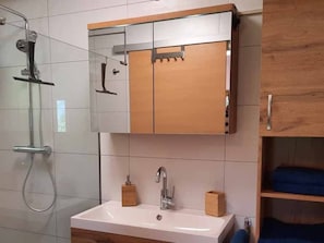 A bathroom with a shower, a sink, a mirror, and wooden cabinets. - Kiwi apartment with balcony - Kiwi vacation apartment (Weyregg am Attersee)