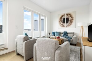Una sala de estar moderna con un sofá gris, una mesa de centro con copas de vino y un televisor sobre un mueble de madera.