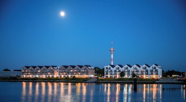 A waterfront hotel with multiple buildings, a prominent tower, and a calm reflective water surface. - OstseeOase - Infrared Sauna, Shower, Fireplace, Rooftop Terrace, Parking Space (Olpenitz)