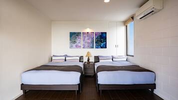 A hotel room with two beds, a nightstand, a lamp, and a wall-mounted air conditioner.