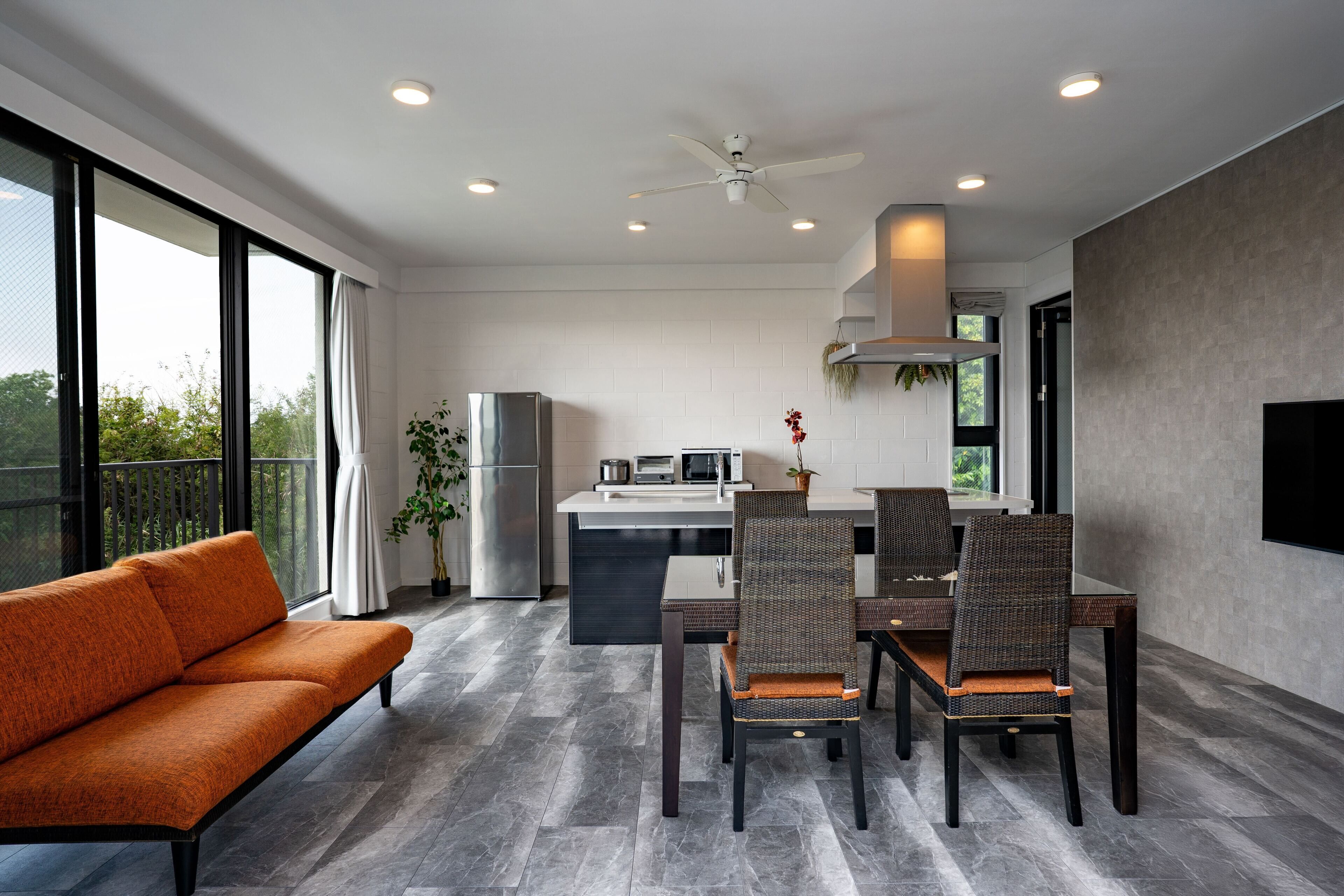 A modern kitchen with a dining area, large windows, and a ceiling fan.