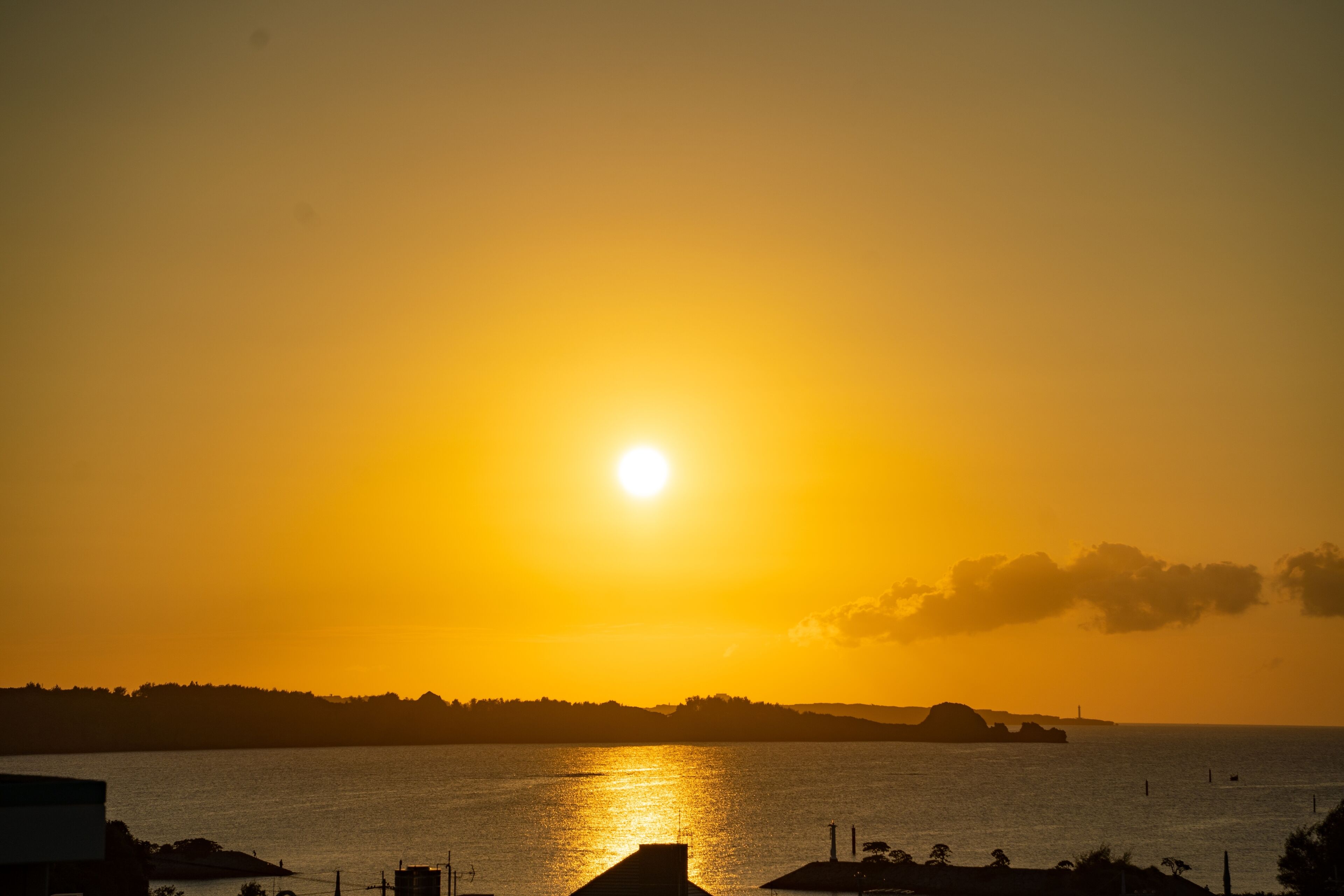 Un coucher de soleil sur une étendue d’eau, avec des bâtiments au premier plan.