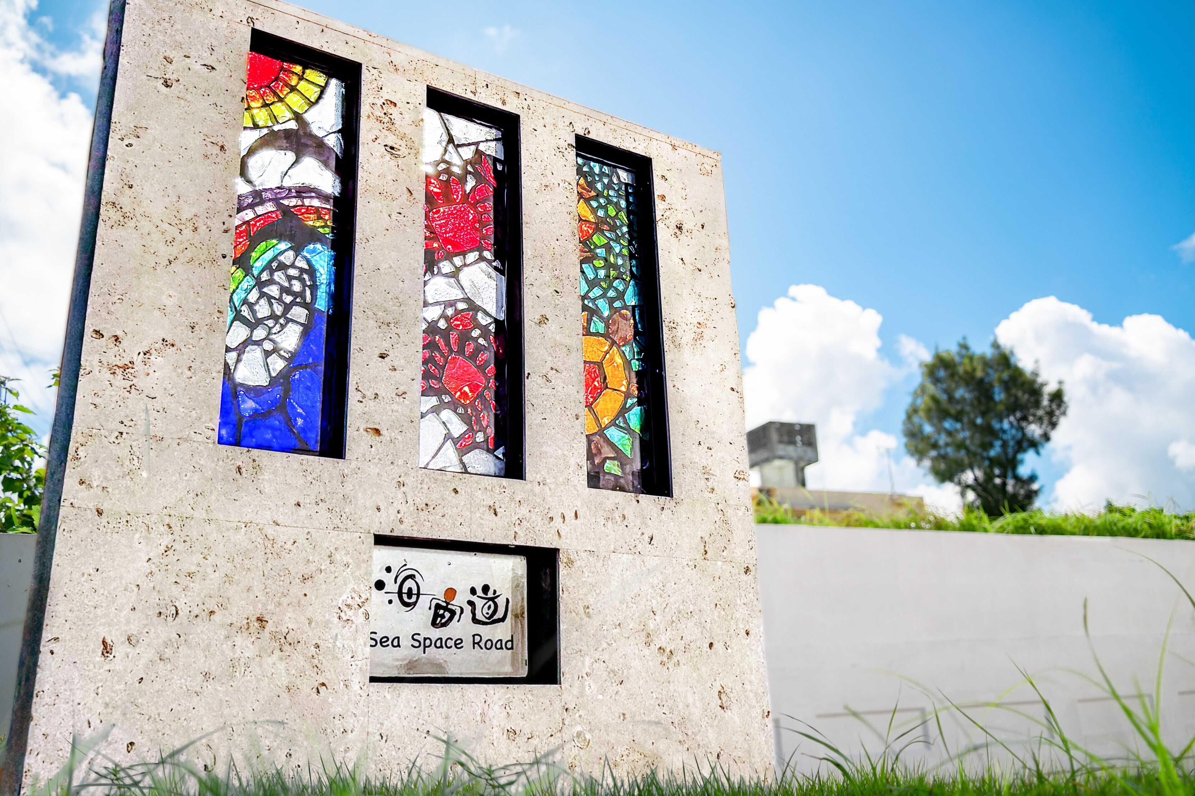 Uma estrutura de concreto com três janelas de vitrais e uma placa com a inscrição 'Sea Space Road'.