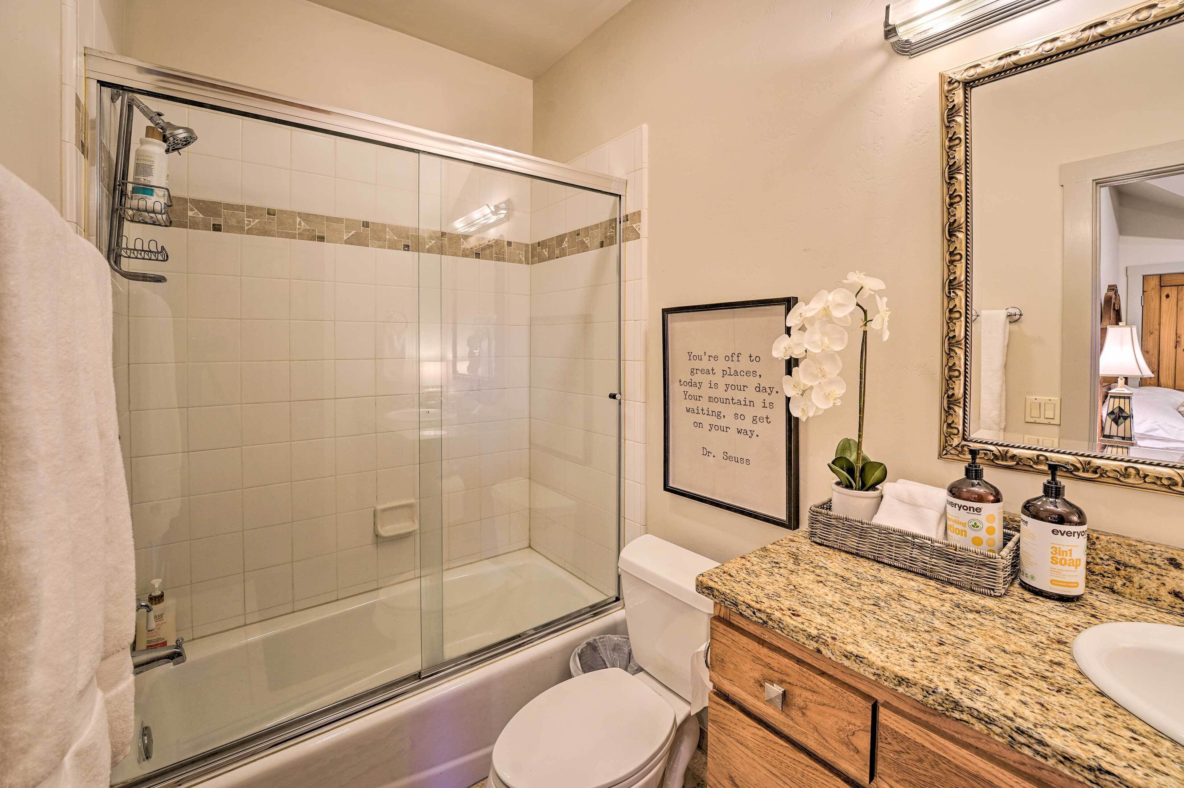 Une salle de bain dotée d’une douche à parois de verre, de toilettes, d’un lavabo avec un plan de travail en granit et d’une citation encadrée au mur.