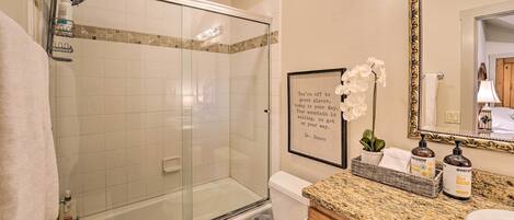 Une salle de bain dotée d’une douche à parois de verre, de toilettes, d’un lavabo avec un plan de travail en granit et d’une citation encadrée au mur.