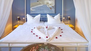 A bed with a heart-shaped towel arrangement and rose petals, a painting of seagulls on the wall, and two bedside lamps. - Pure bliss Mandö, Germany (List)