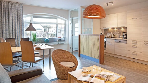 A modern living room with a sofa, dining table, wicker chair, and a magazine on the table. - Pure bliss Mandö, Germany (List)