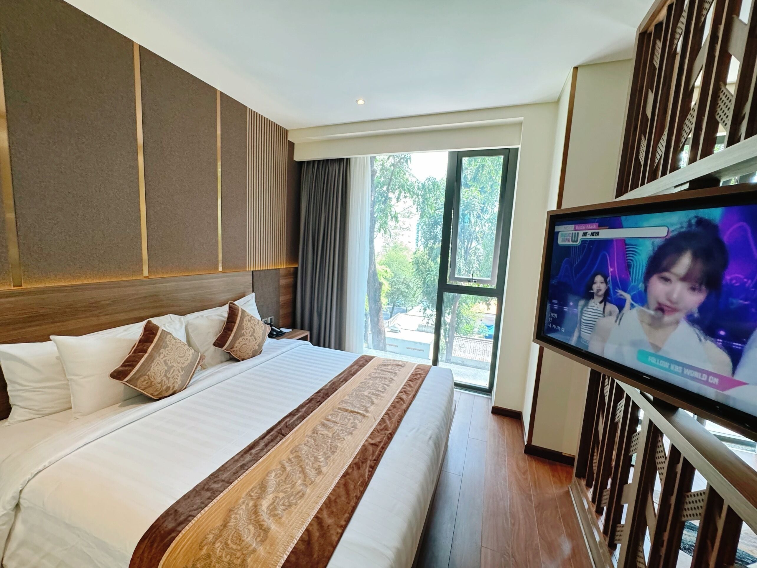 A hotel room with a large bed, a television on the wall, and a view of the outdoors through a glass door.