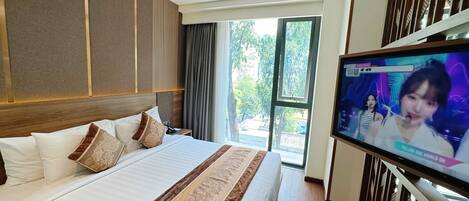 Ein Hotelzimmer mit einem großen Bett, einem Wandtelevisor und Blick ins Freie durch eine Glasdoor.