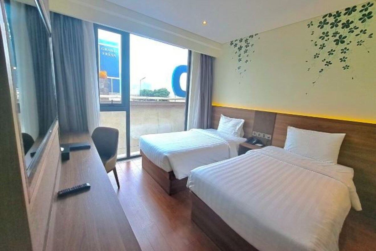A hotel room with two beds, a desk, and a large window.