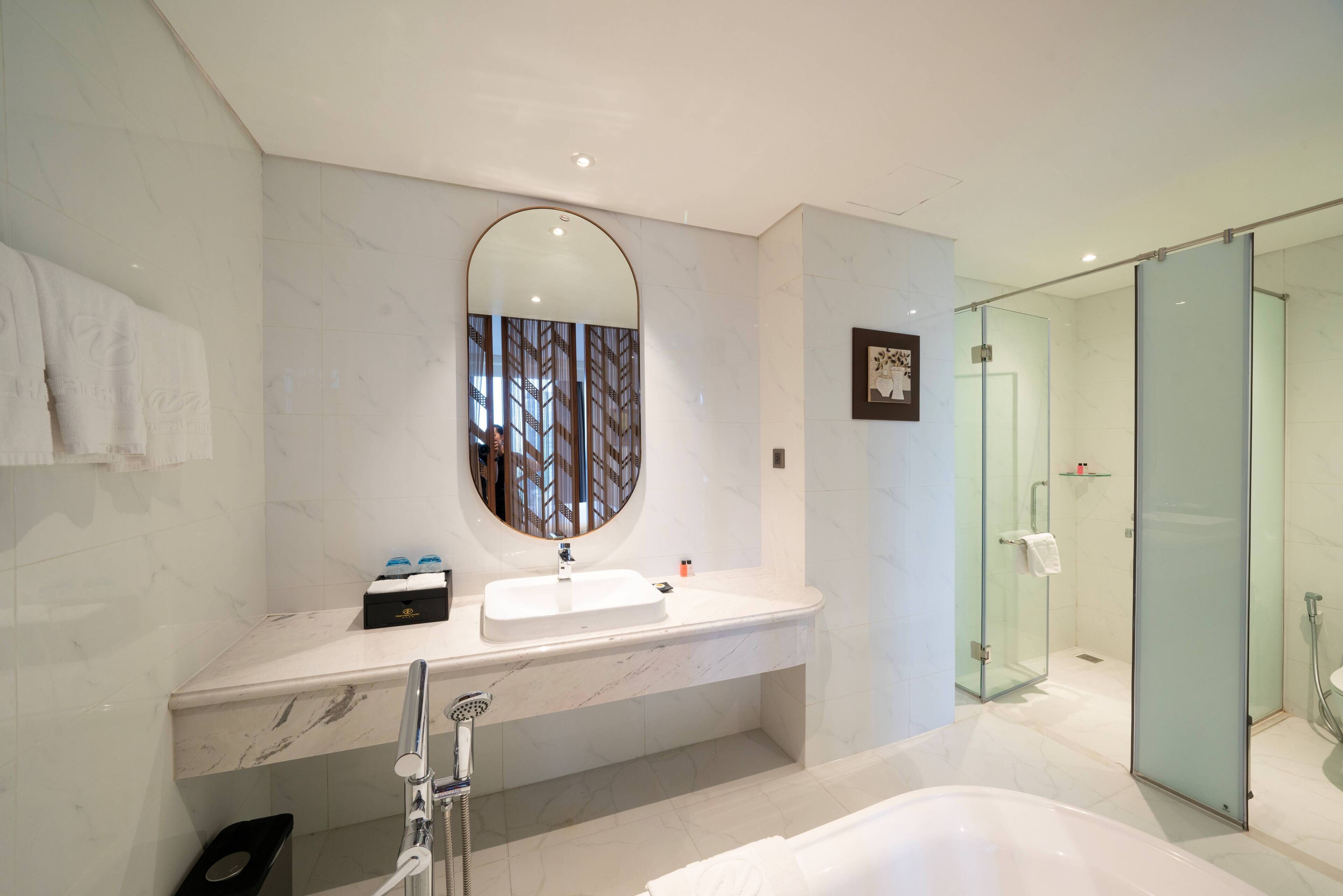 Un baño moderno con lavamanos de mármol, un espejo grande y una ducha con cerramiento de vidrio.