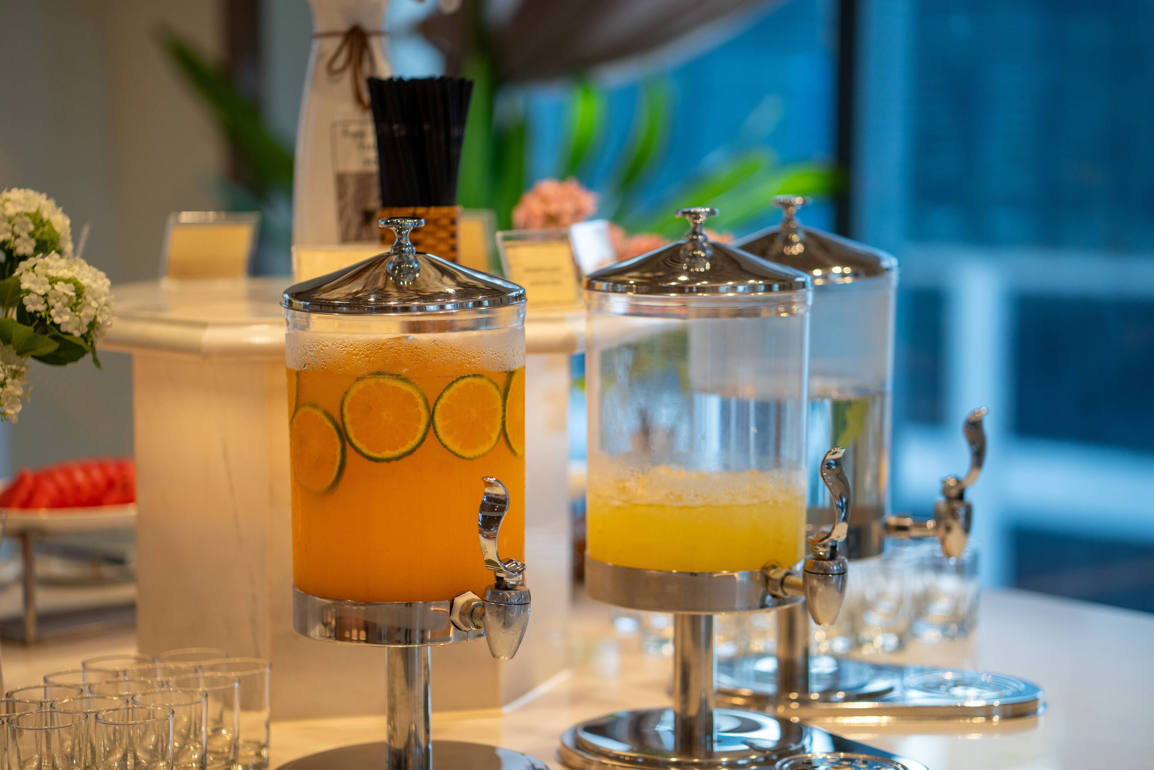 A beverage station with two dispensers, one with a citrus drink and the other with a yellow beverage, both with spouts for pouring.