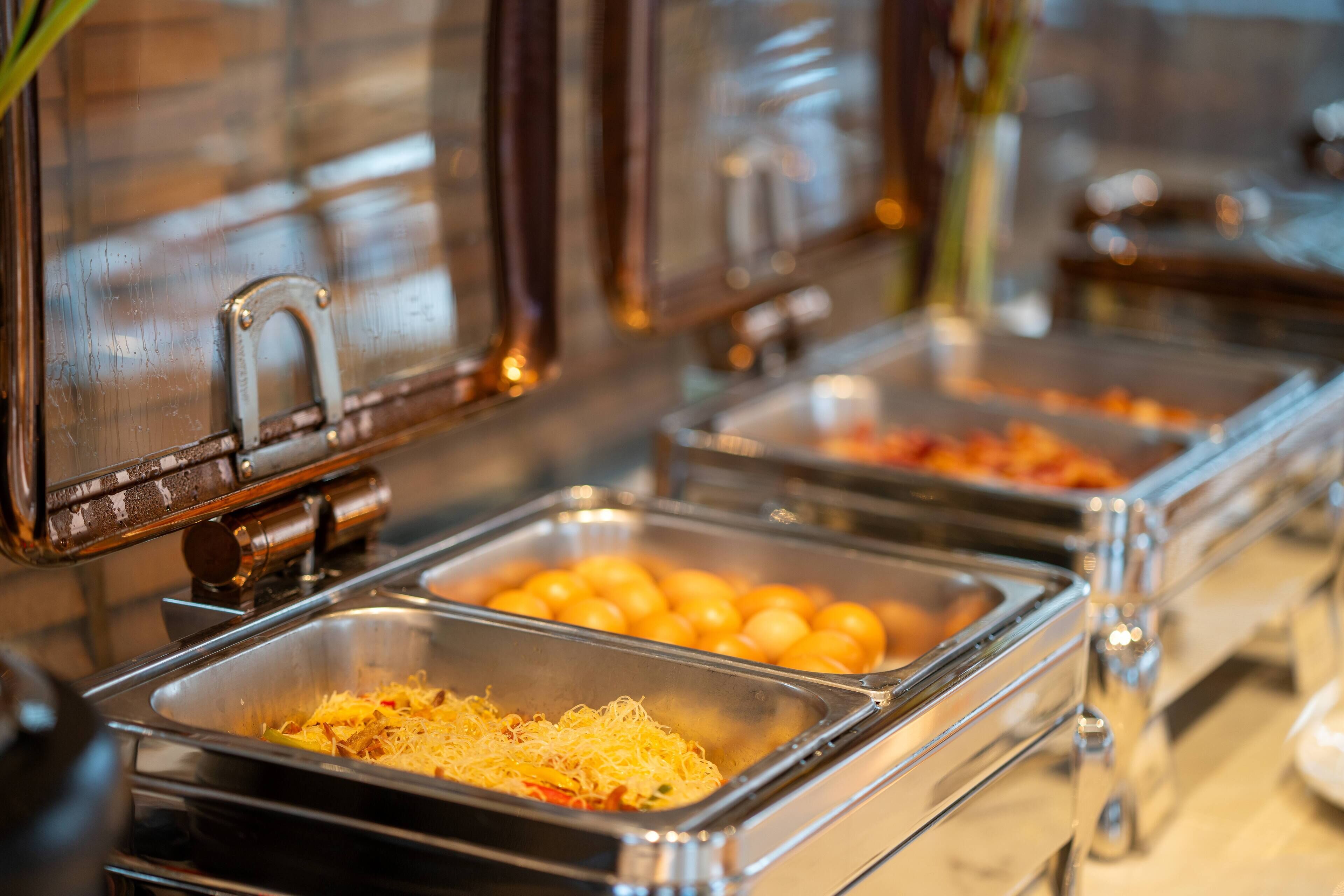 A buffet setup with various food items in metal trays, including what appears to be scrambled eggs and orange fruits.