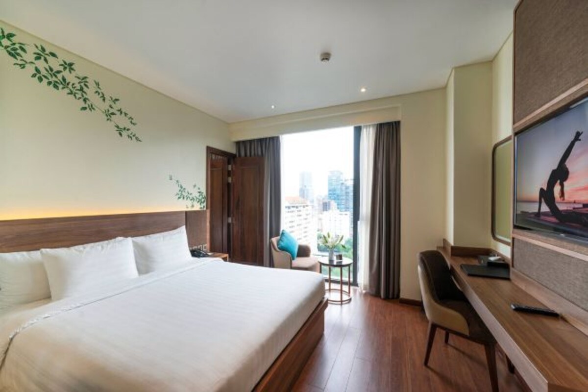 A hotel room with a large bed, a desk, a chair, a TV, and a view of the city.