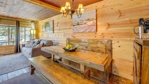 Un interior de cabaña acogedor, con techo de madera, un sofá, una banca y una mesa de comedor.