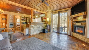Interior acogedor de una cabaña con chimenea, pisos de madera, ventilador de techo y un marco de piedra para la chimenea.