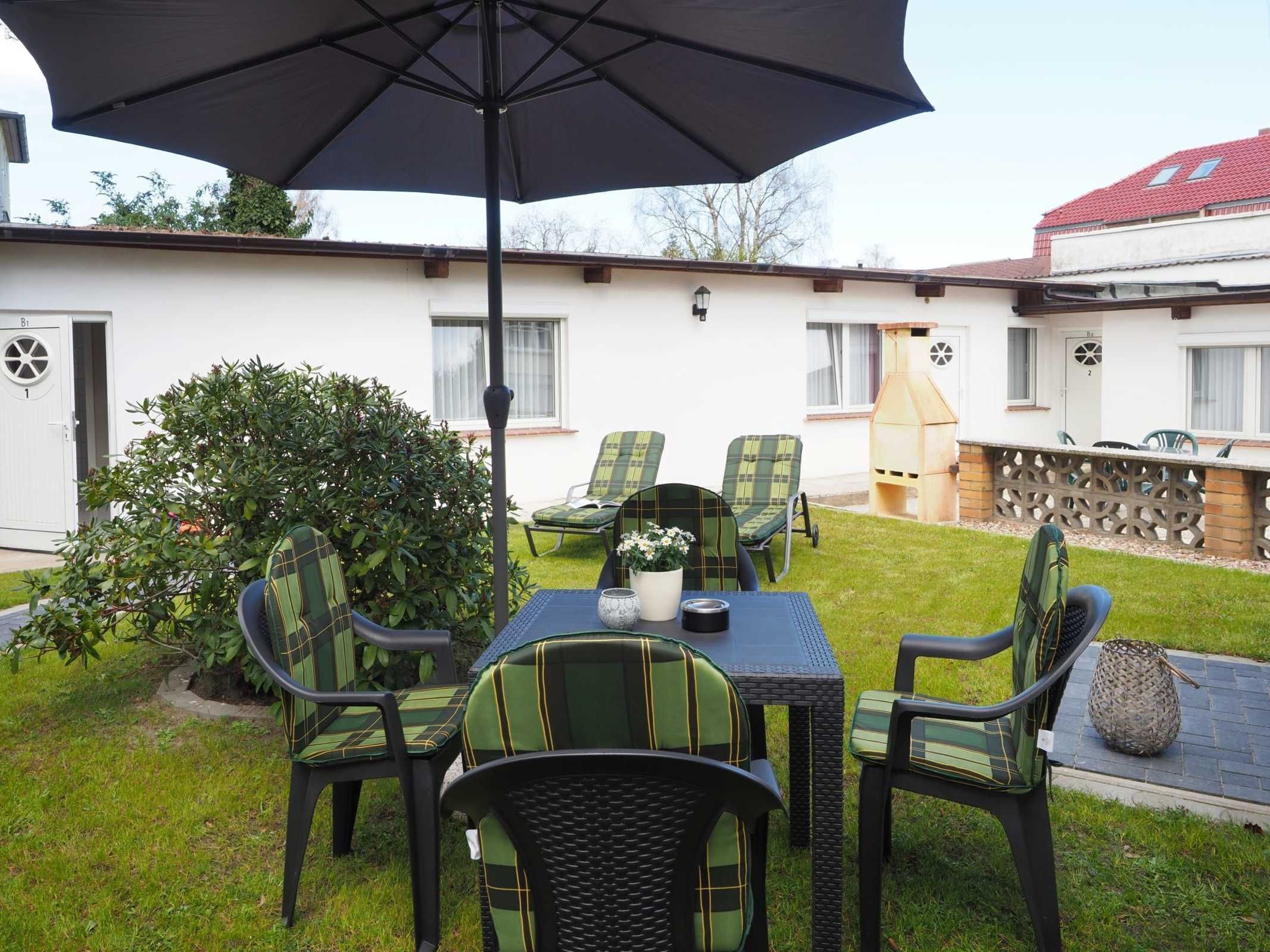 Une terrasse extérieure avec une table et des chaises, un grand parasol et un barbecue.