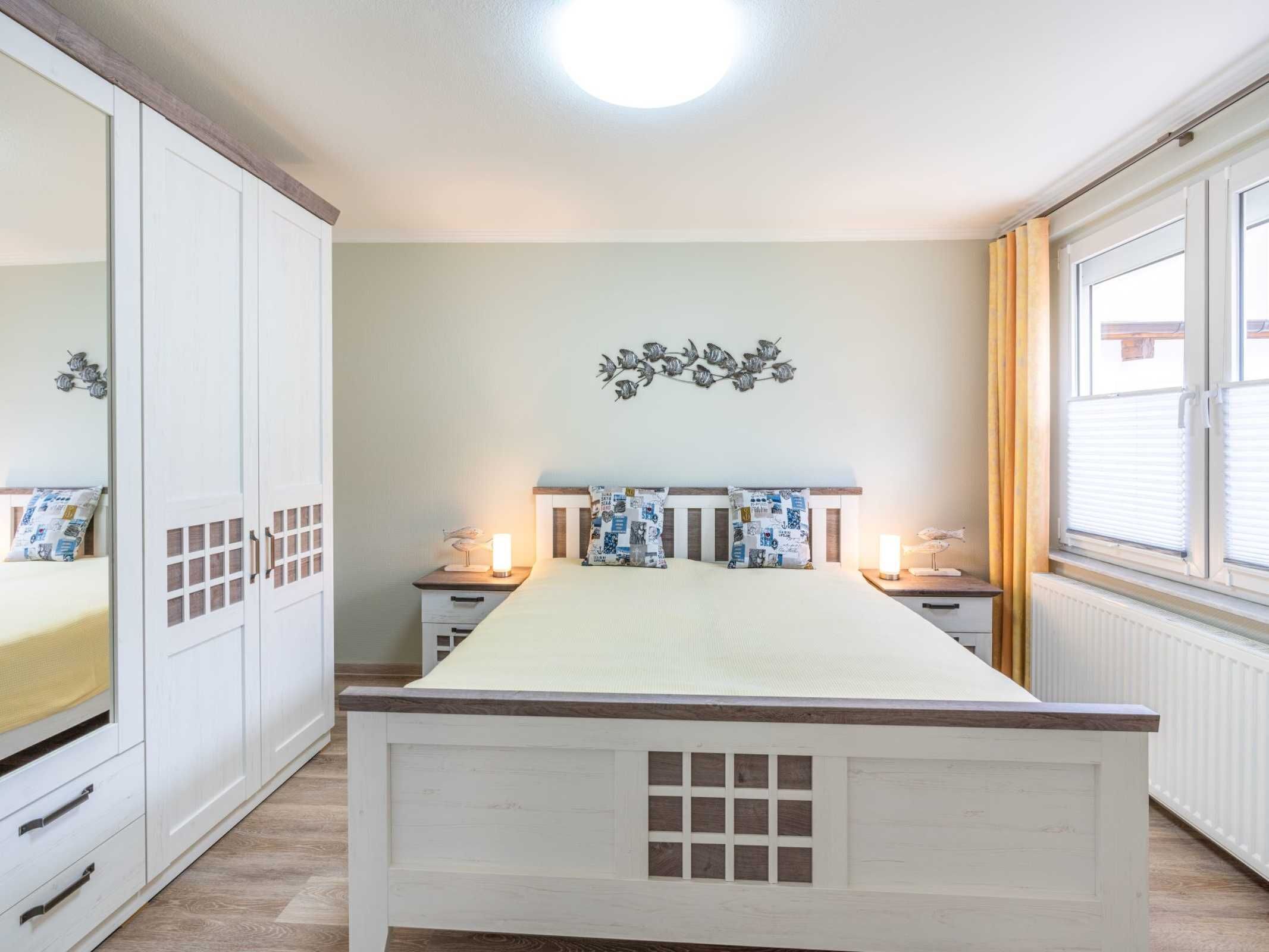 Une chambre à coucher comprenant un lit, des tables de chevet, une armoire et une fenêtre avec des rideaux.