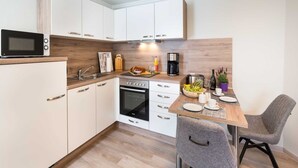 A compact kitchen with white cabinets, a microwave, a coffee maker, and a dining area with a table and chairs. - Ahlbeck Villa Stephanie Bungalow H2AS rear - Ahlbeck Villa Stephanie (Heringsdorf)