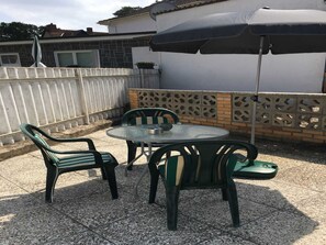 A patio with a round glass table and four chairs, an umbrella, and a white fence. - Ahlbeck Villa Stephanie Bungalow H2AS (rear) - Ahlbeck Villa Stephanie (Heringsdorf)