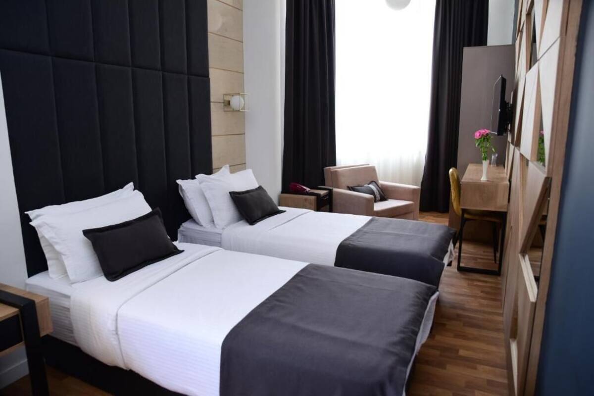 A hotel room with two beds, a desk, a chair, and a TV.