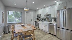 Une cuisine moderne avec des meubles blancs, des appareils en acier inoxydable et un coin repas comprenant une table et des chaises en bois.