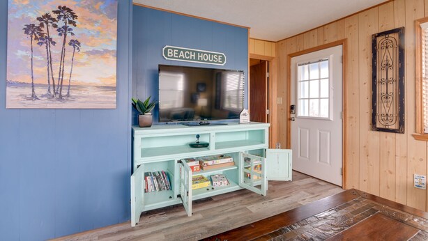 A room with a blue wall, a sign reading "BEACH HOUSE", a television on a light blue cabinet, and a wooden door. - 1/2 Mi to Gulf: Family Home in Crystal Beach! (Crystal Beach)