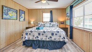 A bedroom with a wooden floor, a ceiling fan, a bed with a blue and white ocean-themed bedspread, two wall-mounted paintings, and a window with blinds. - 1/2 Mi to Gulf: Family Home in Crystal Beach! (Crystal Beach)