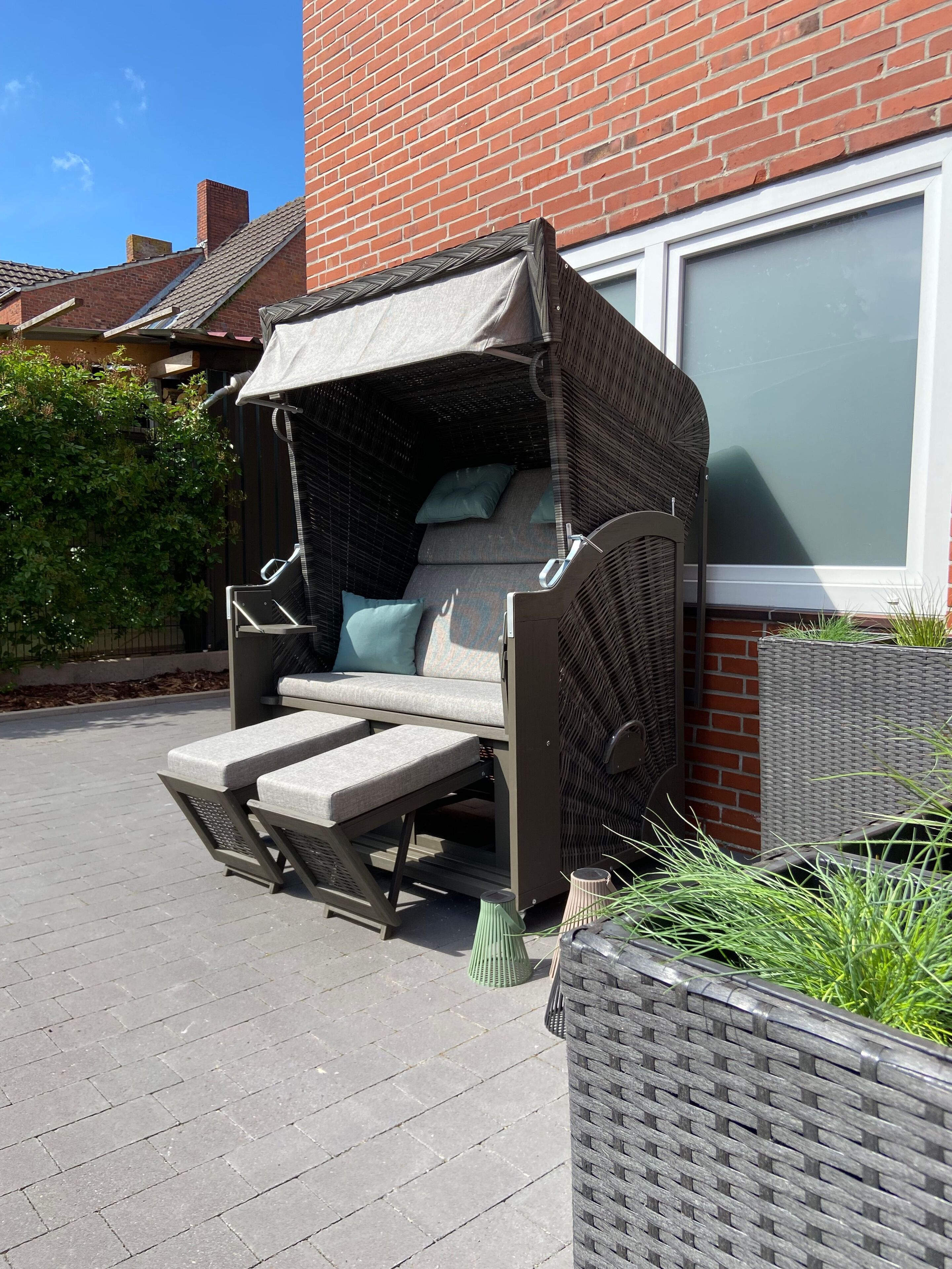 An outdoor wicker sofa with a canopy, positioned against a brick wall with a window.