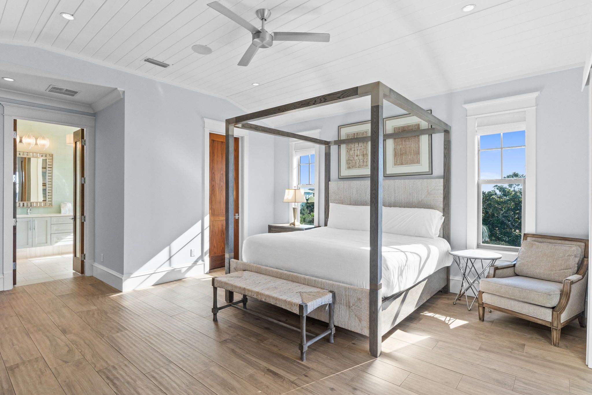 A spacious bedroom with a four-poster bed, a bench, a chair, and a small table.