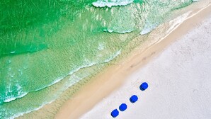 An aerial view of a beach with a sandy shore and a series of blue umbrellas aligned in a row. - 🐬🐟 The Life Aquatic | Pool | Golf Cart | Rooftop Gulf Views | FREE Excursions ☀️ (Destin)