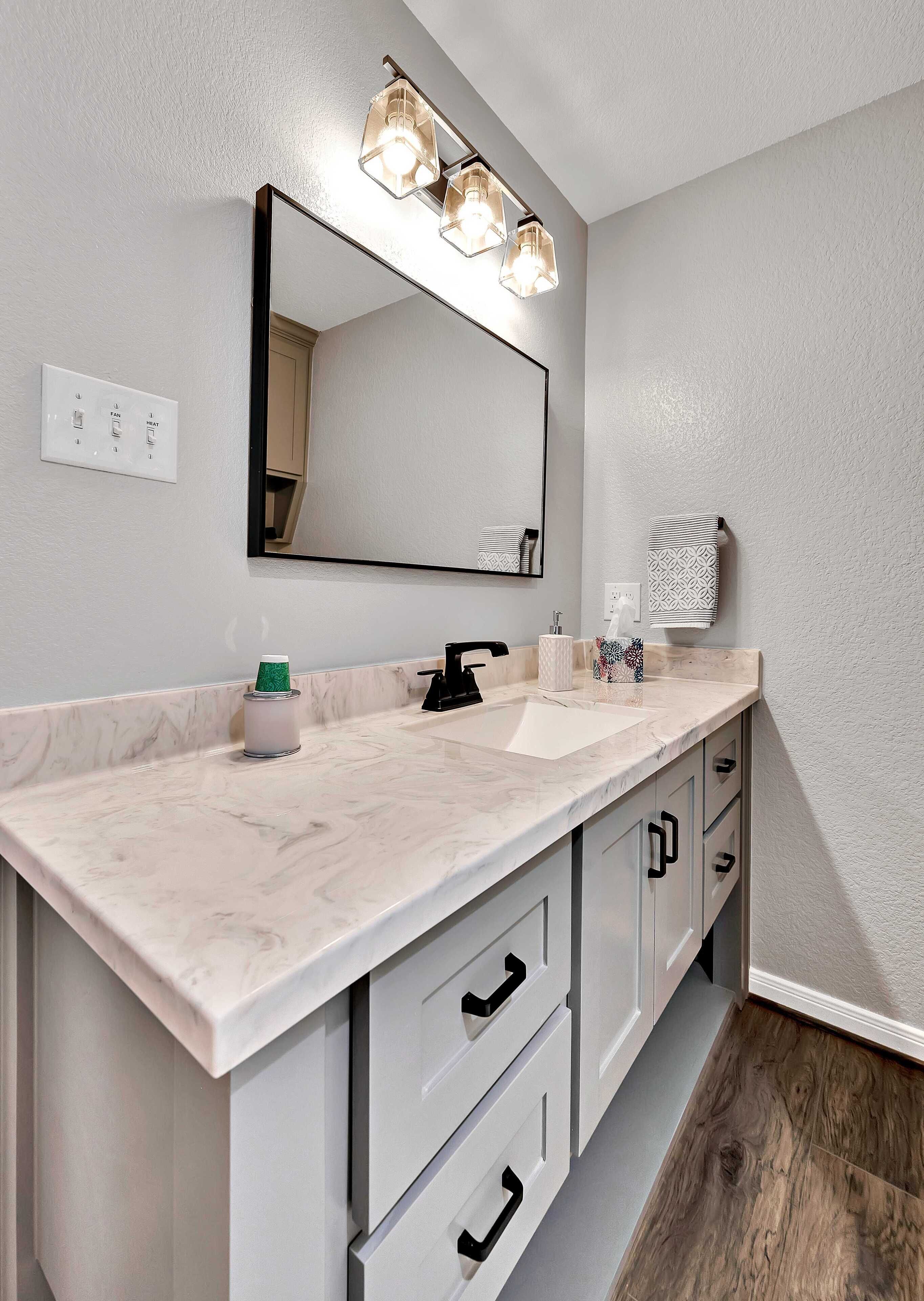 A bathroom with a marble countertop, a sink, a mirror, and a vanity with drawers.