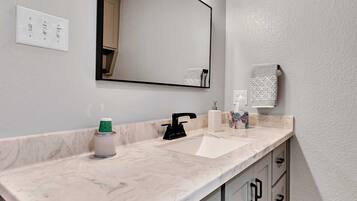 A bathroom with a marble countertop, a sink, a mirror, and a vanity with drawers.