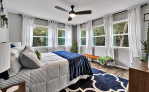 A bedroom with a bed, a ceiling fan, large windows, and a view of trees. - Brazos River Bungalow - Close To Silos & Baylor (Waco)