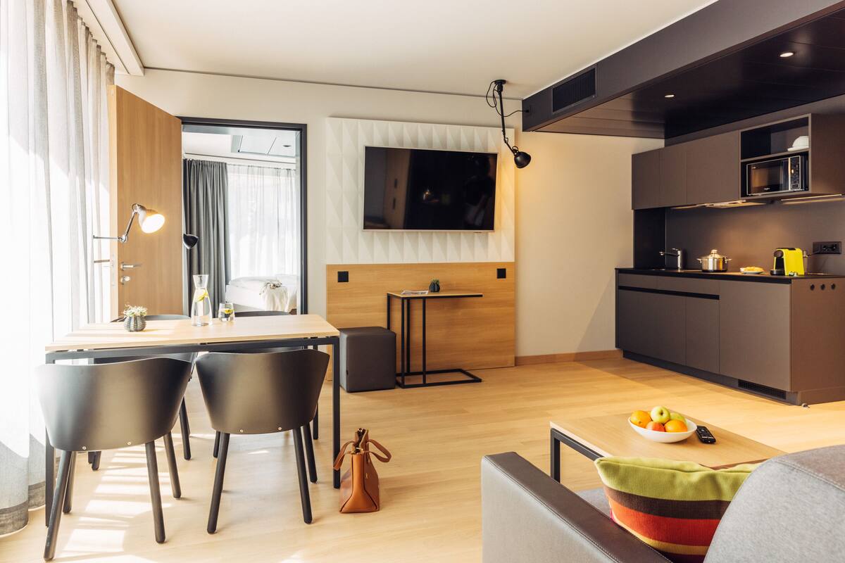 Une cuisine moderne dotée d’un téléviseur à écran plat, de meubles en bois et d’un coin repas avec des chaises et une table.