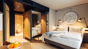 Une chambre d’hôtel moderne dotée d’un grand lit, de tables de chevet, d’un panier de fruits et d’une  œuvre d’art murale originale.